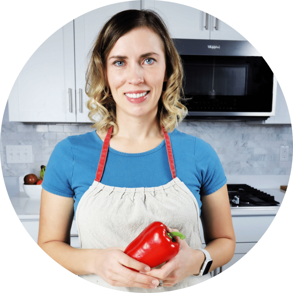 woman in kitchen holding a red bell pepper